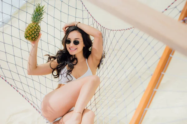 Belle jeune femme souriante en bikini avec ananas relaxant dans un hamac sur la plage — Photo de stock