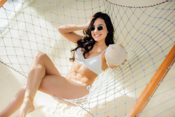 Belle jeune femme heureuse en bikini tenant cocktail de noix de coco et couché dans un hamac sur la plage — Photo de stock