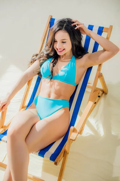 Bela menina sorridente em biquíni relaxante na cadeira deck na praia — Fotografia de Stock