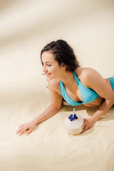 Schöne sexy junge Frau im Bikini mit Kokoscocktail am Strand liegend — Stockfoto