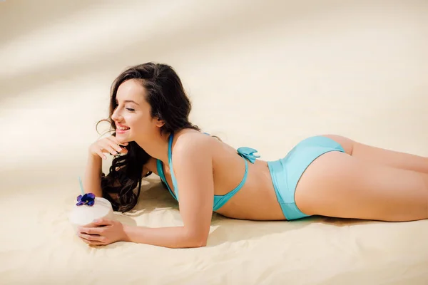 Hermosa chica sexy en bikini con coctel de coco sonriendo y acostado en la playa - foto de stock