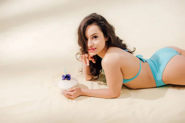 Bella ragazza sexy in bikini con cocktail di cocco guardando la fotocamera mentre sdraiato sulla spiaggia — Foto stock