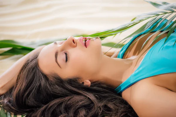 Hermosa chica posando con hoja verde y acostado en la playa con los ojos cerrados - foto de stock