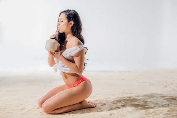 Hermosa chica sentada y beber coctel de coco en la playa con espacio para copiar - foto de stock