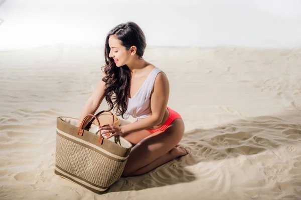 Красивая улыбающаяся молодая женщина с плетеной сумкой на пляже — стоковое фото