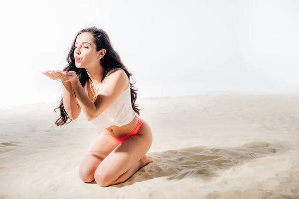 Beautiful girl blowing on sand in hands while sitting on beach with copy space — Stock Photo