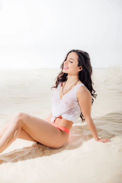 Beautiful sexy girl in wet top sitting, smiling and posing on beach — Stock Photo