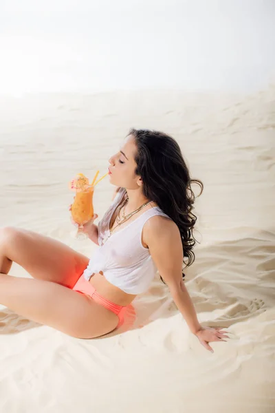 Beautiful girl in white top drinking cocktail on beach — Stock Photo