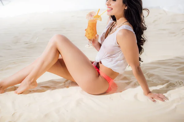 Vista parcial de chica sonriente bebiendo cóctel en la playa - foto de stock