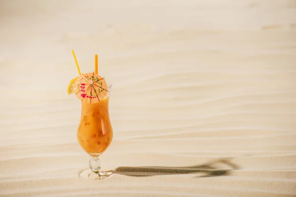 Orange cocktail with cocktail umbrella on sandy beach with copy space — Stock Photo