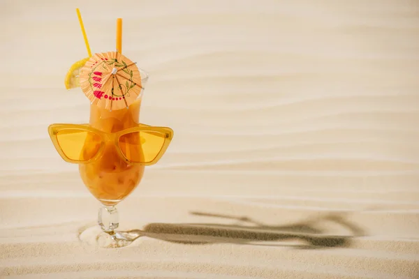 Cóctel naranja con gafas de sol y paraguas de cóctel en la playa de arena con espacio para copiar - foto de stock