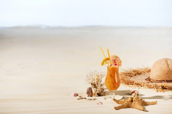 Cocktail, starfish, Straw Hat, coral and sea stones on sandy beach with copy space — Stock Photo