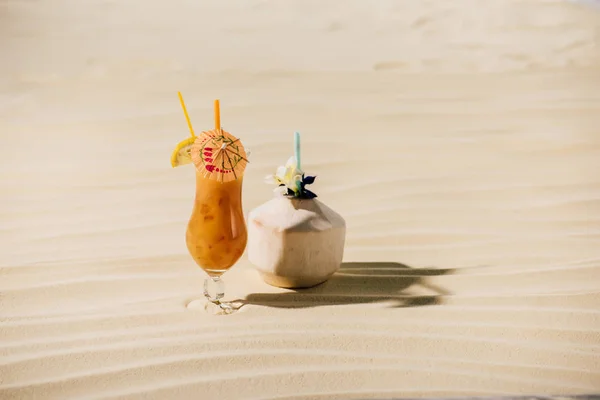 Cocktail in coconut with flower and cocktail in glass on sandy beach — Stock Photo