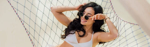 Panoramic shot of beautiful smiling girl in bikini lying in hammock on beach — Stock Photo