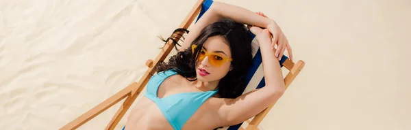 Panoramaaufnahme eines schönen Mädchens im Bikini und Sonnenbrille, das es sich auf einem Liegestuhl am Strand gemütlich macht — Stockfoto
