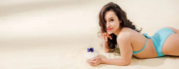 Plano panorámico de hermosa chica en bikini con coctel de coco tumbado en la playa con espacio para copiar - foto de stock
