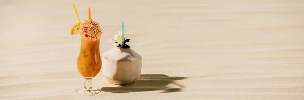 Panoramic shot of cocktail in coconut with flower and cocktail in glass on sandy beach with copy space — Stock Photo