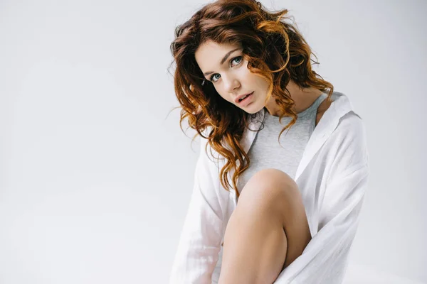 Pretty woman with curly red hair sitting and looking at camera on white — Stock Photo