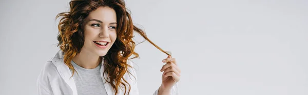 Panoramic shot of cheerful young woman touching red hair on white — Stock Photo