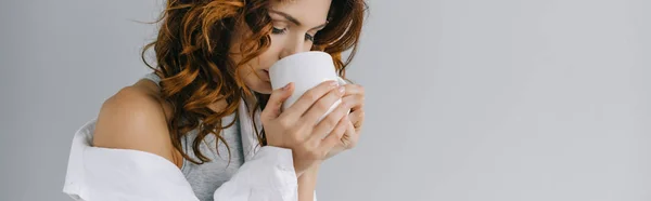 Panoramic shot of pretty curly girl drinking coffee on grey — Stock Photo
