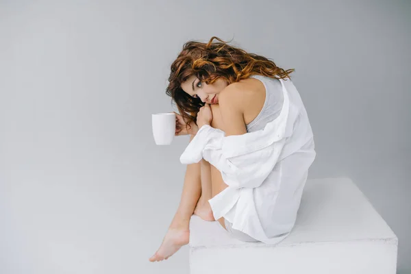 Мрійлива і приваблива молода жінка тримає чашку з кавою на сірому — стокове фото