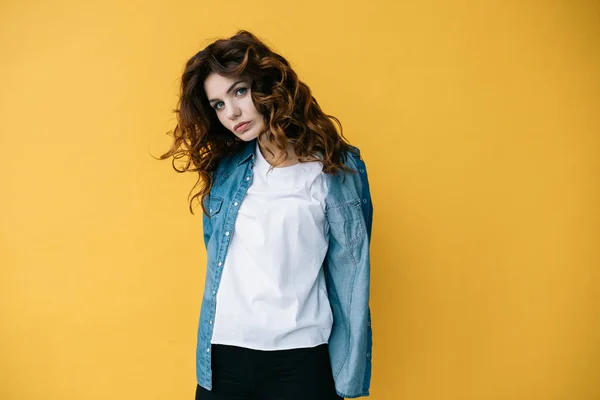 Attractive curly young woman looking at camera and standing on orange — Stock Photo