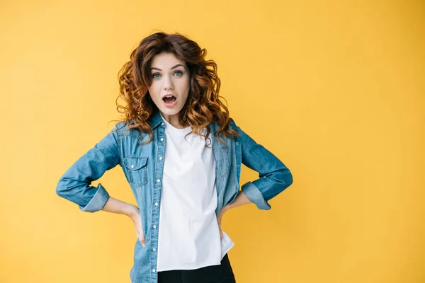 Surprise fille bouclée debout avec les mains sur les hanches et regardant caméra sur orange — Photo de stock