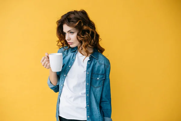 Beautiful young woman with curly red hair holding cup on orange — Stock Photo