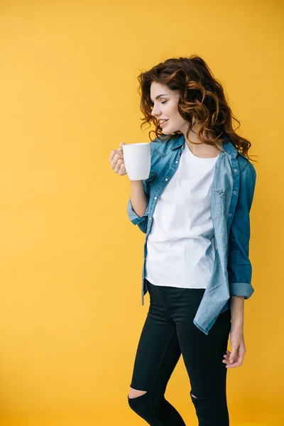 Fröhlich lockige junge Frau mit Tasse und steht auf orange — Stockfoto