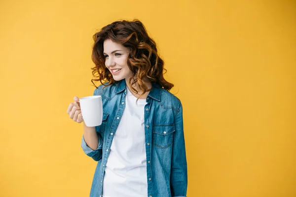 Happy curly young woman holding cup and standing on orange — Stock Photo