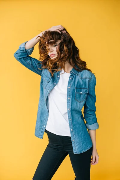 Jolie jeune femme touchant les cheveux roux bouclés tout en se tenant sur orange — Photo de stock