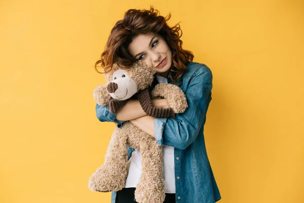 Attraktive lockige rothaarige junge Frau mit Teddybär auf orange — Stockfoto