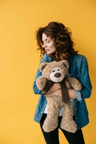 Pretty redhead girl hugging teddy bear and standing with closed eyes on orange — Stock Photo