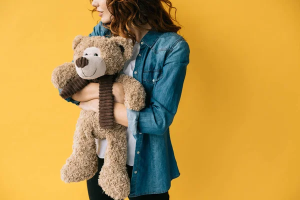Cropped view of redhead girl hugging teddy bear and standing on orange — Stock Photo