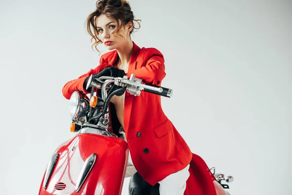 Atractiva y elegante joven sentada en motocicleta roja y mirando a la cámara en blanco - foto de stock