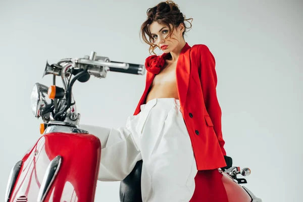 Atractiva joven sentada en motocicleta roja y mirando a la cámara en blanco - foto de stock