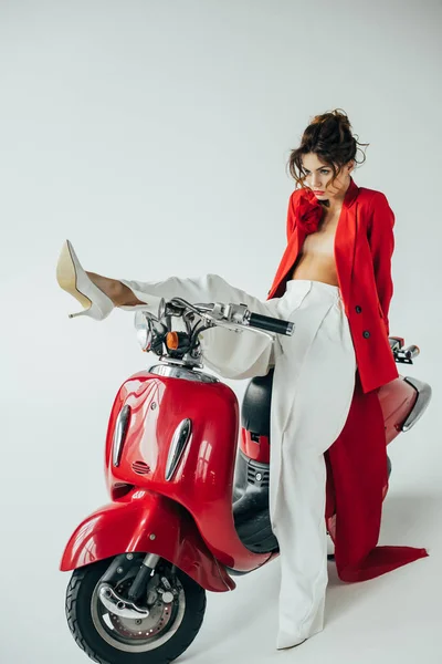 Attractive young woman sitting on red motorcycle and looking at heels on white — Stock Photo
