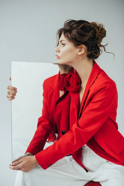 Attraktive rothaarige junge Frau mit Spiegel auf grau — Stockfoto