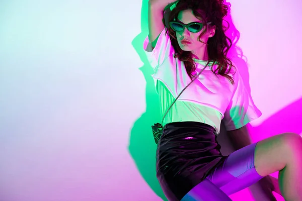 Jeune femme à la mode et belle dans des lunettes de soleil assis sur violet avec dégradé — Photo de stock
