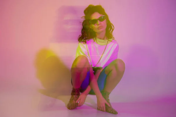 Motion blur of young woman in sunglasses sitting on purple with gradient — Stock Photo