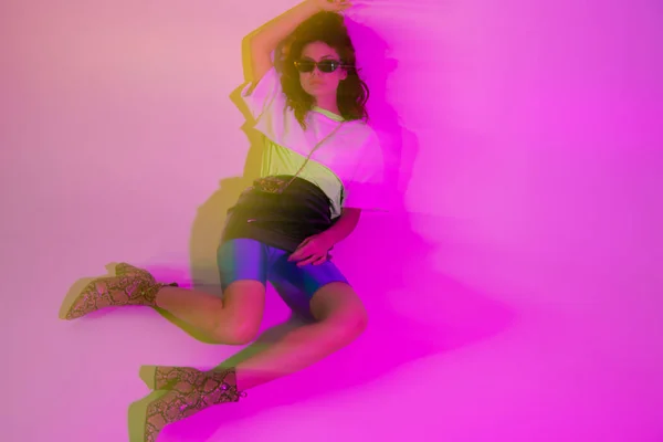 Motion blur of stylish young woman in sunglasses lying on purple — Stock Photo