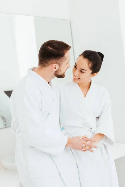Cheerful brunette girl holding hands while looking at boyfriend in bathroom — Stock Photo
