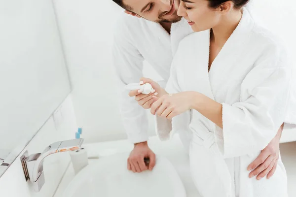 Обрезанный вид бородатого мужчины, смотрящего на девушку, держащую зубную пасту в ванной — стоковое фото