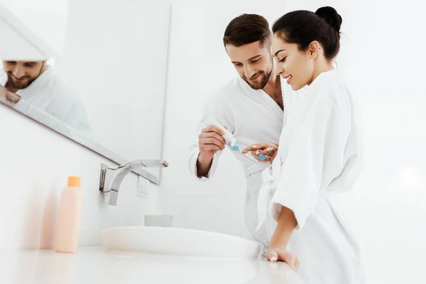 Vista basso angolo di donna allegra guardando l'uomo tenendo spazzolino da denti e dentifricio — Foto stock