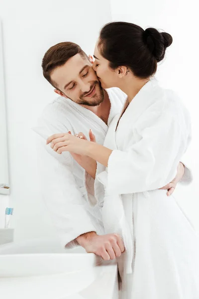 Feliz mujer aplicando crema de manos y besar mejilla en guapo novio - foto de stock