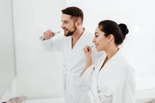 Femme gaie et homme barbu brossant les dents et souriant dans la salle de bain — Photo de stock