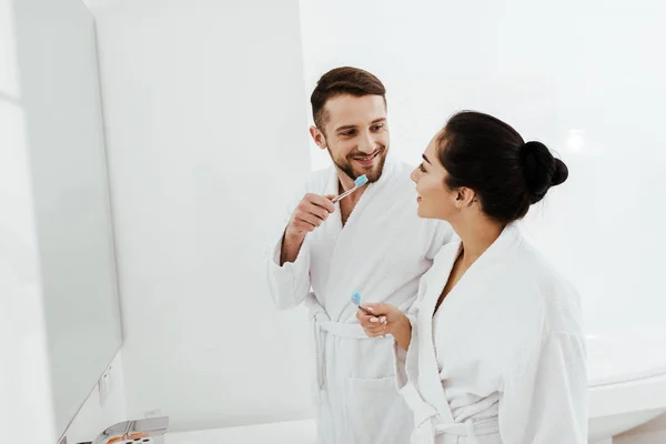 Bonito homem olhando para atraente morena mulher segurando escova de dentes — Fotografia de Stock