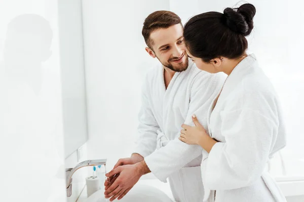 Chica morena tocando albornoz de hombre guapo lavándose las manos — Stock Photo