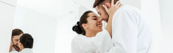 Plano panorámico de chica feliz sonriendo mientras abrazo novio en albornoz - foto de stock