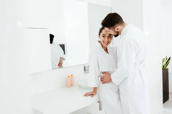 Handsome man hugging happy girlfriend standing and smiling in bathrobe — Stock Photo